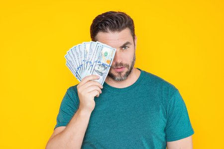 Man holding cash money in dollar banknotes on isolated yellow background. Studio portrait of businessman with bunch of dollar banknotes. Dollar money concept. Career wealth business. Cash dollar.の写真素材