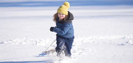Kid boy play in the snow with a winter hat. Happy kid in warm clothes enjoying snow falling. Kid playing in snowy park. Child play with snow outdoors during first snowfall. Winter activities for kids.の写真素材