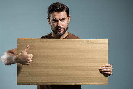 Man holding empty board on studio background. Male model with thumb up showing blank signboard with...