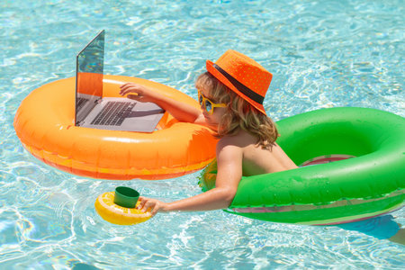 Kid working on laptop computer at poolside swimming pool. Summer online technology. Traveler...