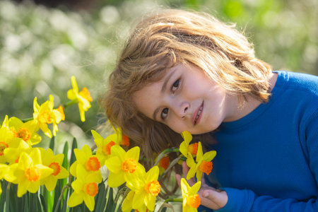 Little kid smelling spring narcissus flower outdoor. Pretty child boy 10 year old with flowers over...