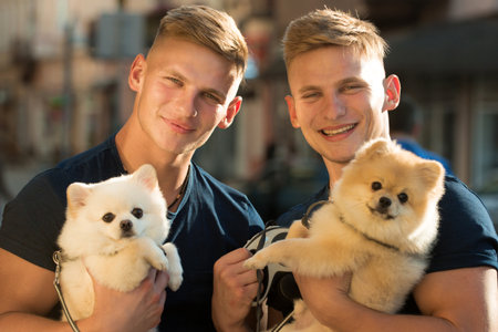 Siblings brothers hold their puppy dogs. Two handsome siblings with cute puppies. Twins and pets. Portrait of siblings brothers outdoor. Men siblings outdoor. Twin boys and puppies.の写真素材