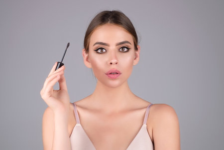 Beautiful woman applies brow gel with brows brush to her eyebrow. Studio portrait of young woman doing her eyebrow natural make up. Eyebrows make up concept.の写真素材