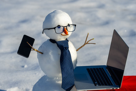 Snowman using smartphone in winter landscape. Funny snowman phone call outdoors. Snowman with laptop. Snowman businessman working on computer. Business man in winter. Winter online technology.の写真素材