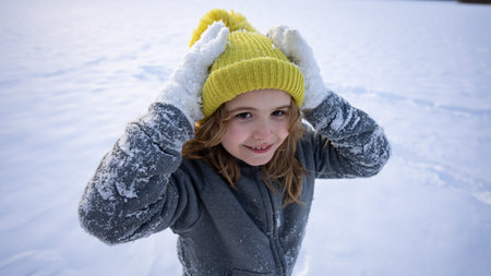 Closeup portrait of a happy child in snow. Portrait of a smiling boy in winter. Kid playing outdoors in frosty weather. Emotional face lit by snowfall. Kid fun in the snow. Funny kids winter face.の写真素材