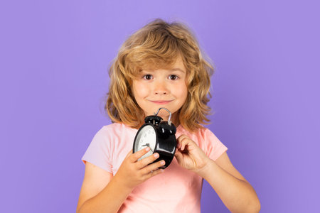 Funny child holding alarm clock with funny face. Morning school time concept with surprised kid....