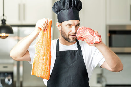 Handsome man cooking fish and meat, salmon and beef in kitchen. Portrait of casual man cooking in the kitchen with fish and meat ingredients. Casual man preparing raw fish and meat in kitchen.の写真素材