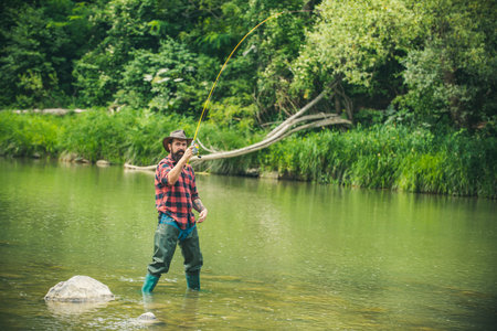 Young man fishing. Fisherman with rod, spinning reel on river bank. Man catching fish, pulling rod while fishing on lake. Wild nature. The concept of rural getaway.の写真素材