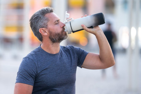 Sport fitness man resting on a bench and drink water from sport water bottle. Mature sport model...