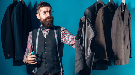 Tailor in his workshop. Suit tailoring. Handsome man is classic tailor. Tailor measuring fabric in a...