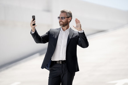 Business portrait. Happy business man using phone outdoors. Successful leader. Man in suit chatting on phone outdoor. Business man hold phone. Businessman using phone. Business online meeting.の写真素材