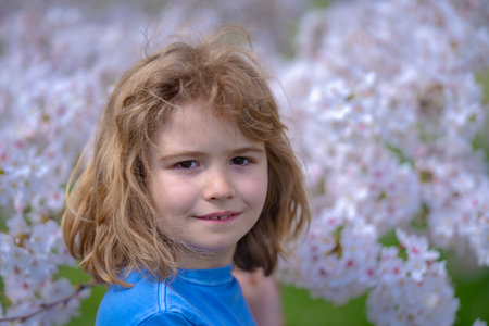 Cute blonde kid boy in spring garden. Little child under a blossom tree. Happy kid playing under blooming cherry tree. Kid with flower on Easter. Adorable kid in blooming cherry garden on spring day.の写真素材