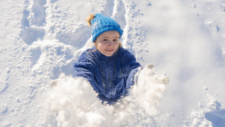 Kid and snow in the park. Kid plays joyfully in snowfall. Winter kids portrait. Snowflakes on happy...
