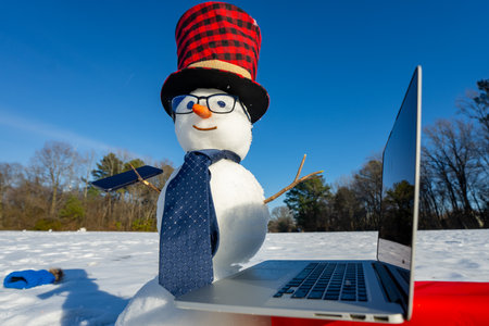 Snowman talking on smartphone in snowy landscape. Snowman making a business phone call. Funny snowman using laptop outdoors. Snowman with mobile phone during winter celebration.の写真素材
