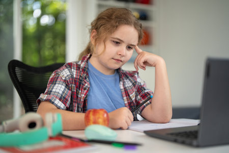 Child learning at home with laptop and books. Kid learning in a cozy home classroom. Kid learning homework. Online learning. Education concept. Child tutoring at home. Boy doing schoolwork.の写真素材