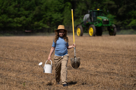 Kid holding a shovel on the farm. Child helps with farm work. Kid working in the farm field. Young farmer on rural field. Field work with kids. Eco kids farm.の写真素材