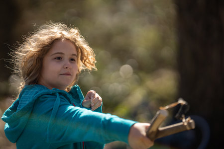 Slingshot in kids hand. Child holding catapult. Kid aiming with sling. Child playing with slingshot. Handmade slingshot. Child aiming practice. Child play with catapult.の写真素材