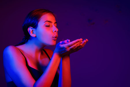 Studio portrait of woman blowing confetti. Portrait of girl on birthday or valentine. Model blow sparkles on birthday. Woman celebrating birthday.の写真素材