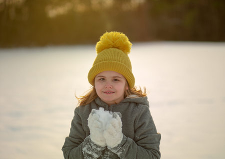 Child play in snowy park. Kid plays in falling snowflakes. Winter fun. Portrait of kid in winter....