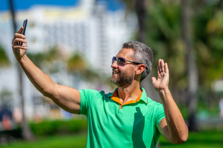 Happy tourist takes a selfie near palm tree. Man captures a selfie during summer vacation. Traveler snaps a selfie in a tropical destination. A selfie with palm trees captures the tropical vibes.の写真素材