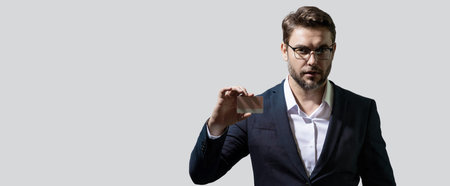 Credit card. Caucasian millennial successful 40s business man holding banking card isolated on gray background, studio portrait. People lifestyle concept. Banner for header, copy space.の写真素材