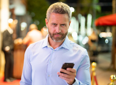 Business man talking on phone on night street. Business man using mobile. Mature businessman chatting online. Businessman making a call. Urban business. Business man speaking on phone outdoors.の写真素材