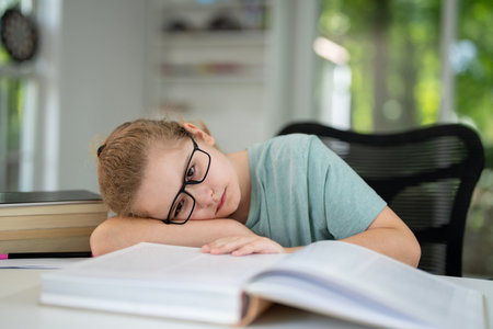 Tired child reading book at desk. Sleepy kid read book at home. Kid yawning while reading homework. Child tired from reading stories. Tired kid studying and reading book.の写真素材