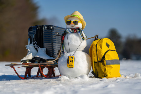 Winter Vacation. Snowman with suitcase ready for winter vacation. Snow man traveler holding travel bag. Funny snowman on winter holiday adventure. Winter journey with a festive snowman.の写真素材