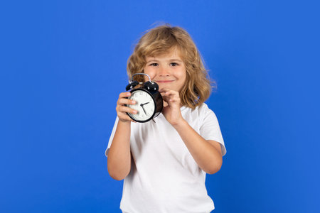 Funny child holding alarm clock with funny face. Morning school time concept with surprised kid....