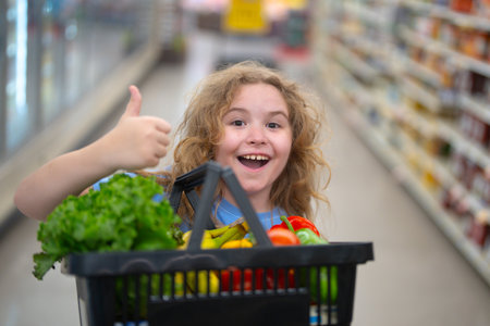 Child in grocery store. Child with shopping cart full of veggies. Kid choosing vegetables in grocery . Child shopping in grocery. Grocery shop fun for kids. Child in fruit market.の写真素材