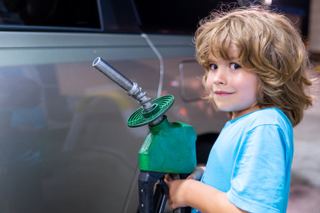 Happy child refueling retro car at gas station. Kid holding fuel nozzle during road trip. Portrait of little traveler with gasoline pump. Childhood vacation moment at petrol station.の写真素材