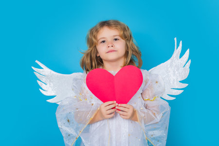 Angel kid with heart. Kid wearing angel costume white dress and feather wings. Innocent child. Little angel on isolated studio background.の写真素材