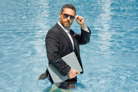 Funny business. Remote job by beach. Summer vacation with laptop. Freelance summer business. Business humor. Handsome businessman in suit swim in water. Relaxing after job. Success and crazy business.の写真素材