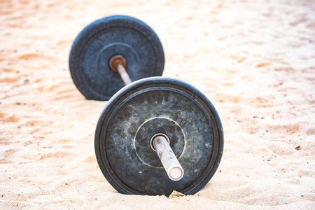 Barbell sport equipment. Sport background. Barbell on sand for summer sport. Barbell in sand background.の写真素材