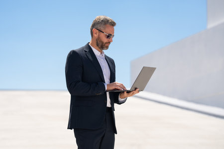 Businessman using laptop outdoors. Successful man working on laptop. Confident businessman with laptop. Business online. businessman checking data on laptop outside. Businessman in suit work online.の写真素材