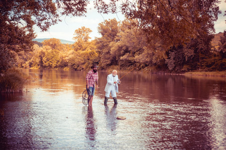 Mature senior man with friend fishing. Summer vacation. Happy cheerful people. Bearded men catching fish. Fisherman with fishing rod. Activity and hobby.の写真素材