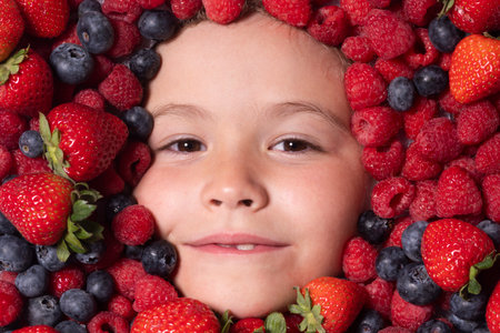 Summer fruits. Berries with kids face close-up. Top view of child face with berri. Berry set near kids face. Cute little boy eats berries. Kid eating vitamins. Close up kids face.の写真素材