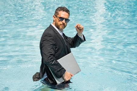 Crazy Business man in suit resting in swimming pool. Crazy summer freelancer working in pool. Funny businessman with laptop on sea beach. Guy enjoying travel and beach. Creative online strategy.の写真素材