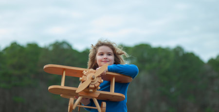 Happy child play with wooden plane outdoor. Child playing with toy airplane. The dream of becoming a pilot. Happy child playing with toy airplane in park. Child dreams of traveling. Kid pilot aviator.の写真素材