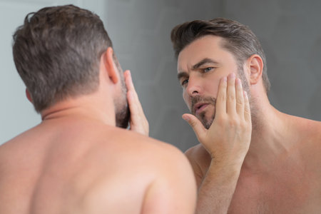 Mens beauty cosmetics, male beauty and skincare. Morning healthcare and hygiene for man. Perfect beauty skin. Handsome millennial man after shower apply nourishing facial cream or mask on skin.の写真素材