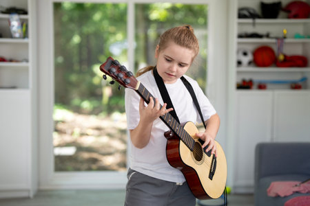 Teen playing acoustic guitar. Child practicing guitar in living room. Young guitarist learning music indoors. Boy strumming guitar during music lesson. Kid playing guitar at room.の写真素材