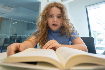 Surprised child reading book. Schoolkid studying and reading. Smart kid read book. Little student learning from book. Child reading book in library. Education and Learning. Knowledge through reading.の写真素材