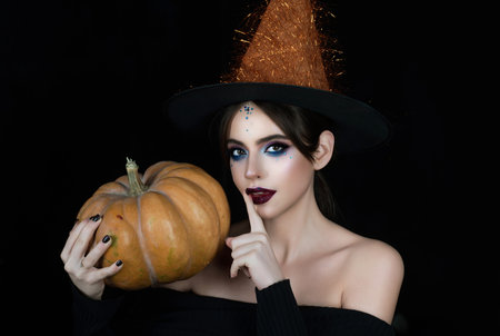 Halloween sexy woman portrait. Halloween sensual girl in witch hat. Halloween pretty woman face with makeup. Halloween beauty woman portrait holding pumpkin.の写真素材