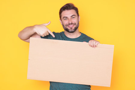 Happy man with blank banner isolated on studio background. Portrait of attractive man with empty blank poster. Man showing poster, pointing finger on signboard placard. Billboard or banner concept.の写真素材