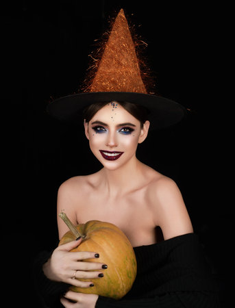 Halloween girl with makeup and witch hat. Halloween witch posing with pumpkin. Halloween party banner. Woman portrait with pumpkin. Halloween witch character. Model in witch costume.の写真素材