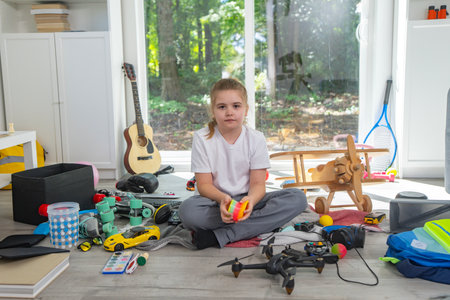 Kid cleaning toys at home. Kid tidying up messy playroom. Kid organizing toys in living room. Kid cleaning scattered toys on floor. Child tidy up children room. Child doing household chores with toys.の写真素材