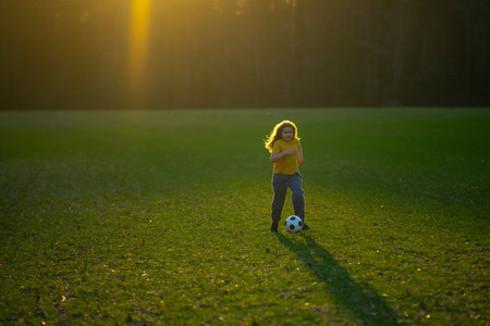 Active child playing football. Kid boy kicking a football on the grass. Child running with a soccer...