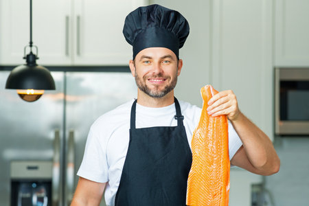 Middle aged man cooking fish salmon in kitchen. Chef on kitchen with fish salmon. Health, natural protein concept. Healthy food concept. Healthy diet.の写真素材