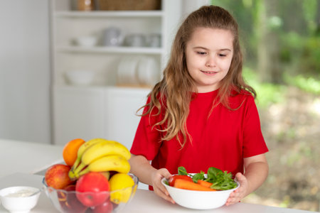Childhood concept. Happy child eating fresh fruits in home kitchen. Cute child eating vegetarian meal in cozy kitchen. Kid eating tasty homemade food in white kitchen.の写真素材