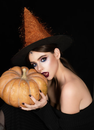 Halloween girl holding pumpkin. Young woman witch posing in studio. Witchcraft theme with woman with...